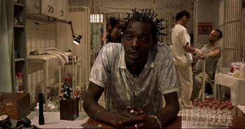 Movie still from “Carandiru” (2003), directed by Hector Babenco – A man sitting at a table in a jail cell; Close Up shot, Low angle