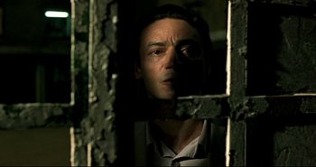 Movie still from “Carandiru” (2003), directed by Hector Babenco – A man standing in a dark room looking out a window; Close Up shot, Low angle