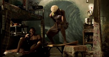 Movie still from “Carandiru” (2003), directed by Hector Babenco – A man sitting on top of a surfboard next to a woman; Wide shot, Low angle