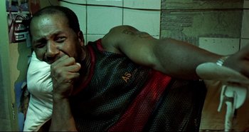 Movie still from “Carandiru” (2003), directed by Hector Babenco – A man in a red and black shirt laying on the ground; Close Up shot, Overhead angle