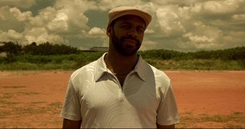 Movie still from “Carandiru” (2003), directed by Hector Babenco – A man wearing a hat standing on a dirt field; Close Up shot, Low angle