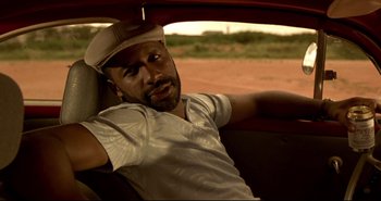 Movie still from “Carandiru” (2003), directed by Hector Babenco – A man sitting in the back seat of a car wearing a hat; Close Up shot, Over the shoulder angle