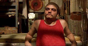 Movie still from “Carandiru” (2003), directed by Hector Babenco – A man in a red tank top and a brown hat; Close Up shot, Low angle