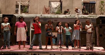 Movie still from “Carandiru” (2003), directed by Hector Babenco – A group of young girls singing on a stage; Wide shot, Low angle
