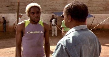 Movie still from “Carandiru” (2003), directed by Hector Babenco – A man in a purple shirt and a man in a blue shirt talking to another man in a purple shirt; Medium shot, Over the shoulder angle