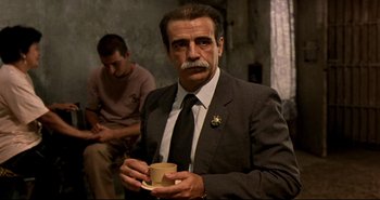 Movie still from “Carandiru” (2003), directed by Hector Babenco – An older man in a suit and tie holding a coffee cup; Medium shot, Over the shoulder angle