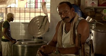 Movie still from “Carandiru” (2003), directed by Hector Babenco – A man sitting next to a pot in a kitchen; Medium shot, Low angle
