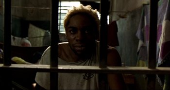 Movie still from “Carandiru” (2003), directed by Hector Babenco – A man in a jail cell looking through the bars; Close Up shot, High angle