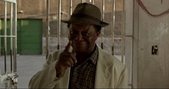 Movie still from “Carandiru” (2003), directed by Hector Babenco – An older man wearing a hat and pointing to his ear; Close Up shot, Low angle