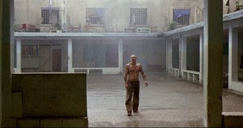 Movie still from “Carandiru” (2003), directed by Hector Babenco – A man walking in the rain with no shirt on; Wide shot, Low angle