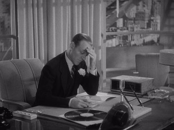 Movie still from “Carefree” (1938), directed by Mark Sandrich – A man sitting at a desk with a book in his hand; Medium shot, High angle