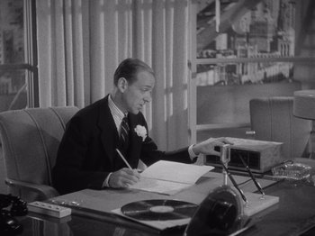Movie still from “Carefree” (1938), directed by Mark Sandrich – A man sitting at a desk writing on a piece of paper; Medium shot, High angle