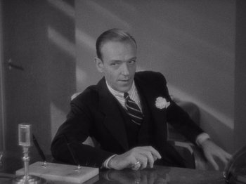 Movie still from “Carefree” (1938), directed by Mark Sandrich – A man sitting at a desk in a suit and tie; Medium shot, High angle