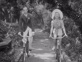 Movie still from “Carefree” (1938), directed by Mark Sandrich – A man and a woman riding bikes down a path; Medium shot, High angle