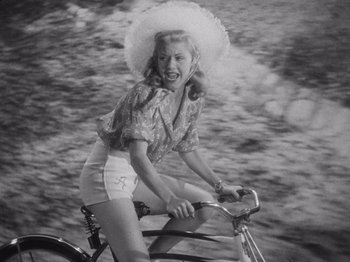 Movie still from “Carefree” (1938), directed by Mark Sandrich – A woman riding a bike with a hat on; Medium shot, High angle