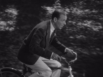Movie still from “Carefree” (1938), directed by Mark Sandrich – A black and white photo of a man riding a bicycle; Medium shot, High angle