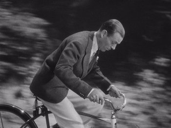 Movie still from “Carefree” (1938), directed by Mark Sandrich – A black and white photo of a man riding a bicycle; Medium shot, High angle