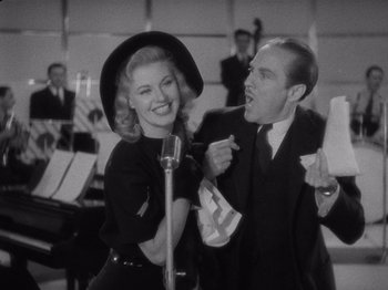 Movie still from “Carefree” (1938), directed by Mark Sandrich – A man and a woman singing into microphones in front of a crowd; Medium shot, Low angle