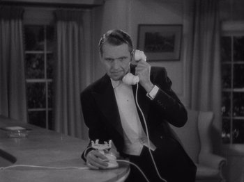 Movie still from “Carefree” (1938), directed by Mark Sandrich – A black and white photo of a man in a suit holding a phone; Medium shot, High angle
