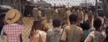 Movie still from “Carmen Jones” (1954), directed by Otto Preminger – A group of young men standing next to each other in front of a fence; Wide shot, High angle