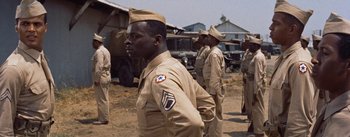 Movie still from “Carmen Jones” (1954), directed by Otto Preminger – A group of men standing next to each other on a dirt field; Medium shot, Over the shoulder angle