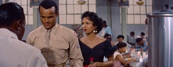 Movie still from “Carmen Jones” (1954), directed by Otto Preminger – A man and a woman walking in front of a crowd; Medium shot, Over the shoulder angle