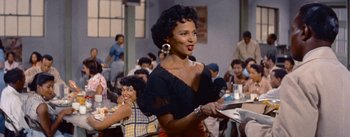 Movie still from “Carmen Jones” (1954), directed by Otto Preminger – A woman in a black dress holding a plate in front of a group of people in a room; Medium shot, Over the shoulder angle