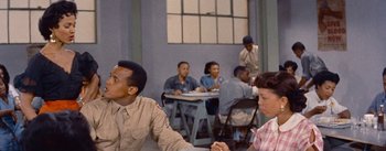 Movie still from “Carmen Jones” (1954), directed by Otto Preminger – A group of people sitting at a table in a room; Medium shot, Over the shoulder angle