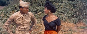 Movie still from “Carmen Jones” (1954), directed by Otto Preminger – A woman in a black top is talking to a man in an army uniform; Medium shot, High angle