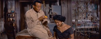 Movie still from “Carmen Jones” (1954), directed by Otto Preminger – A man and a woman sitting next to each other holding an orange; Medium shot, Over the shoulder angle