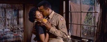 Movie still from “Carmen Jones” (1954), directed by Otto Preminger – A man and a woman kissing in front of a window; Medium shot, Low angle