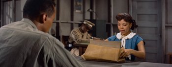Movie still from “Carmen Jones” (1954), directed by Otto Preminger – A couple of people sitting at a table with a bag; Medium shot, High angle