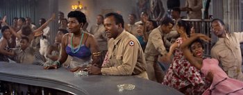 Movie still from “Carmen Jones” (1954), directed by Otto Preminger – A group of people sitting at a table with drinks; Medium shot, Over the shoulder angle
