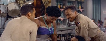 Movie still from “Carmen Jones” (1954), directed by Otto Preminger – A group of people standing around talking to each other in a bar; Medium shot, Over the shoulder angle