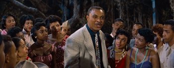 Movie still from “Carmen Jones” (1954), directed by Otto Preminger – A group of people standing around a man wearing a suit; Medium shot, Low angle