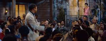 Movie still from “Carmen Jones” (1954), directed by Otto Preminger – A group of people sitting in front of a building; Wide shot, Over the shoulder angle