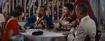 Movie still from “Carmen Jones” (1954), directed by Otto Preminger – A group of people sitting at a table with drinks; Medium shot, High angle