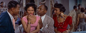Movie still from “Carmen Jones” (1954), directed by Otto Preminger – A group of people sitting around a table; Medium shot, High angle