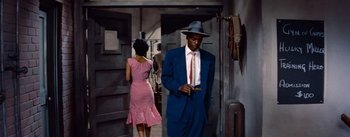 Movie still from “Carmen Jones” (1954), directed by Otto Preminger – A painting of a man in a suit and a woman in a pink dress; Medium shot, Low angle