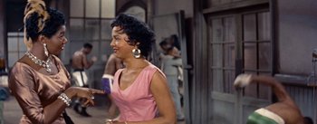 Movie still from “Carmen Jones” (1954), directed by Otto Preminger – A woman in a pink dress is holding a book; Medium shot, Over the shoulder angle