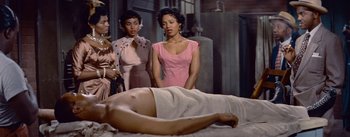 Movie still from “Carmen Jones” (1954), directed by Otto Preminger – A man laying on a bed with three women; Medium shot, High angle