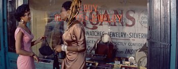 Movie still from “Carmen Jones” (1954), directed by Otto Preminger – A woman with dreadlocks walking past a store window; Medium shot, Low angle