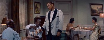 Movie still from “Carmen Jones” (1954), directed by Otto Preminger – A man standing in a room with another man sitting at a table; Medium shot, High angle