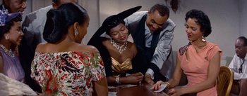 Movie still from “Carmen Jones” (1954), directed by Otto Preminger – A group of people standing around a table; Medium shot, Over the shoulder angle