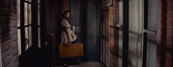 Movie still from “Carmen Jones” (1954), directed by Otto Preminger – A woman standing in a doorway holding a suit case; Wide shot, Low angle