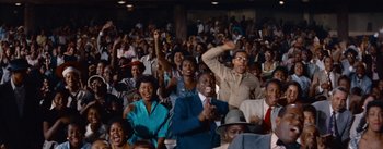Movie still from “Carmen Jones” (1954), directed by Otto Preminger – A group of people sitting in a stadium with their hands in the air; Wide shot, High angle