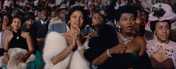Movie still from “Carmen Jones” (1954), directed by Otto Preminger – A group of people sitting in a crowd wearing fur; Close Up shot, Low angle