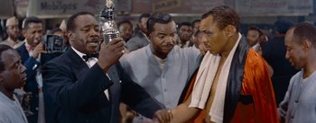 Movie still from “Carmen Jones” (1954), directed by Otto Preminger – A man holding a microphone in front of a crowd; Medium shot, Low angle