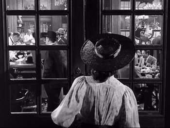 Movie still from “Carrie” (1952), directed by William Wyler – A woman wearing a cowboy hat looking out a window; Medium shot, Over the shoulder angle