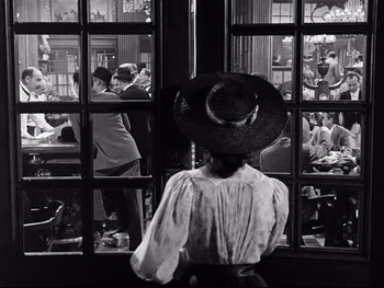 Movie still from “Carrie” (1952), directed by William Wyler – A woman wearing a hat looking out of a window; Medium shot, Over the shoulder angle